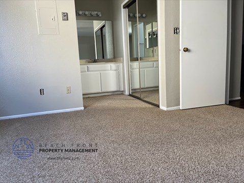 A carpeted room with a door and a mirror.